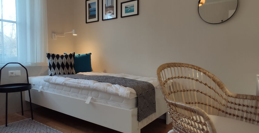 Hell eingerichtetes Einzelzimmer mit Bett und Sessel