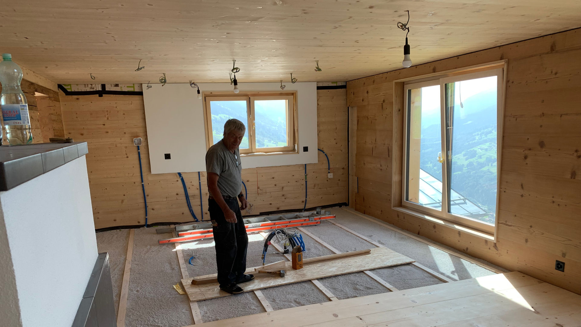 A man working inside a wooden room, windows visible, Zimmereibetrieb, wood flooring.