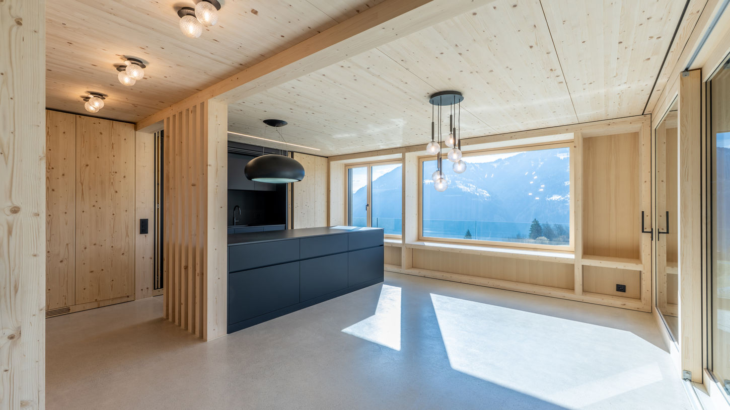 Offene moderne Küche mit dunkler Kochinsel in einem Massivholzhaus-Innenausbau.