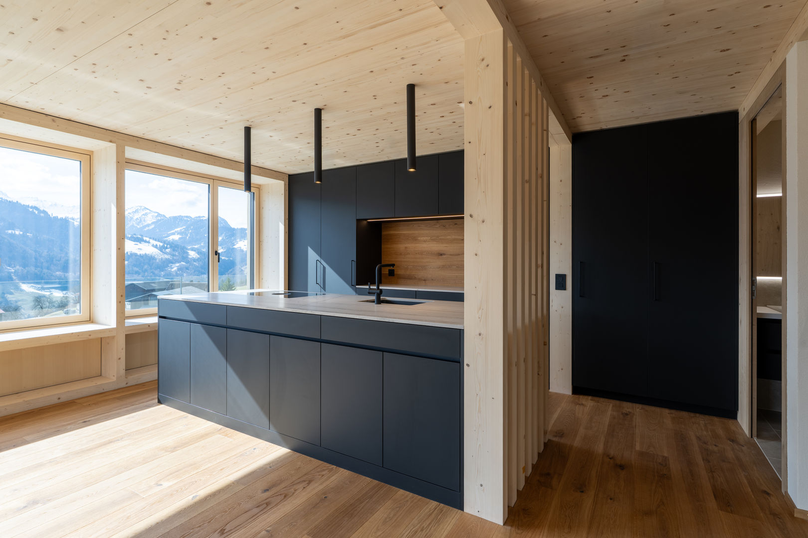 Offene moderne Küche mit dunkler Kochinsel in einem Massivholzhaus-Innenausbau.
