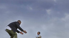 Against a moody, blue sky, Jocephus Martin a Black man with brown skin crouches as a smiling Black boy, Miles-Garvey, runs toward his open ams.