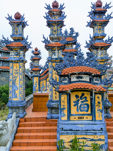Colorful, ornate grave structures with intricate dragon designs and arches. Visible text and a serene, historical atmosphere. Vietnam