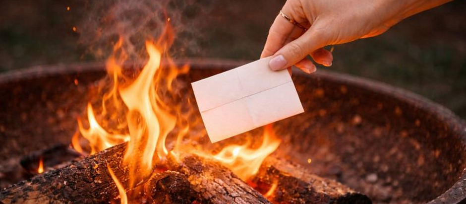 a woman's hand throwing paper into a fire pit