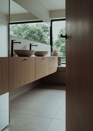 Lichte badkamer met houten maatwerk en uitzicht op de groene omgeving.