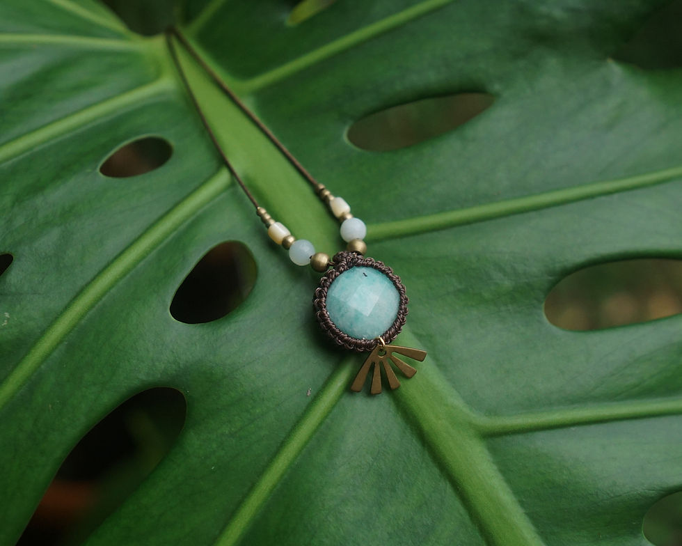A necklace with a blue gemstone pendant on a Monstera leaf. The pendant features gold accents, with lush green hues in the background.