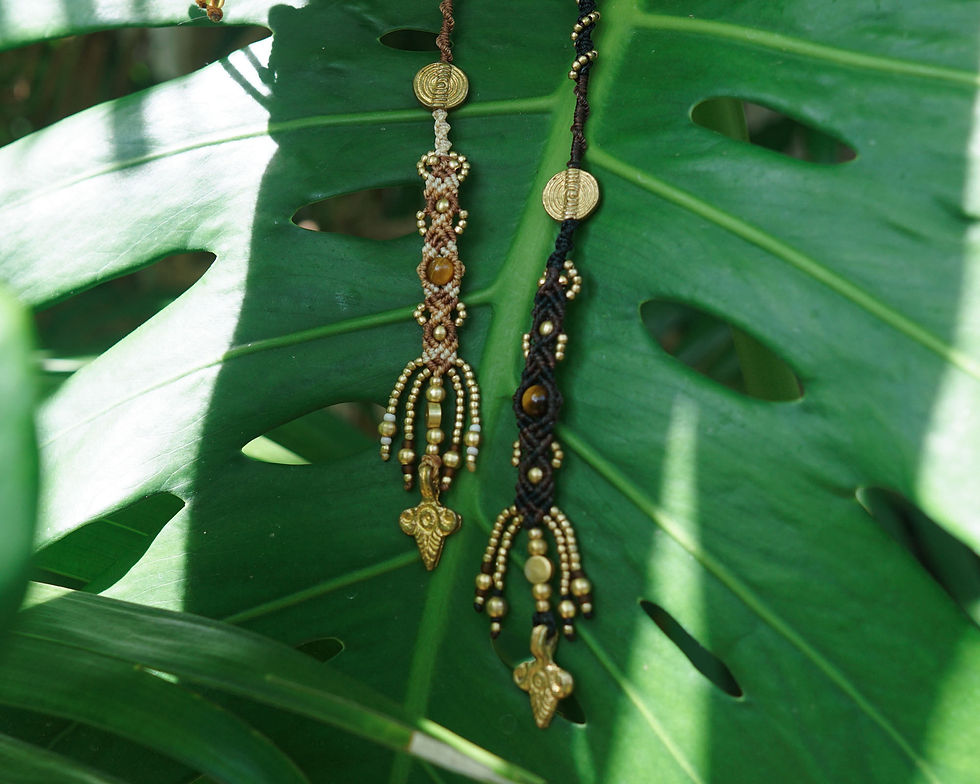 Two intricate handmade hair wraps with beaded designs hang on a vibrant green leaf, dappled with sunlight, creating a peaceful, natural setting.