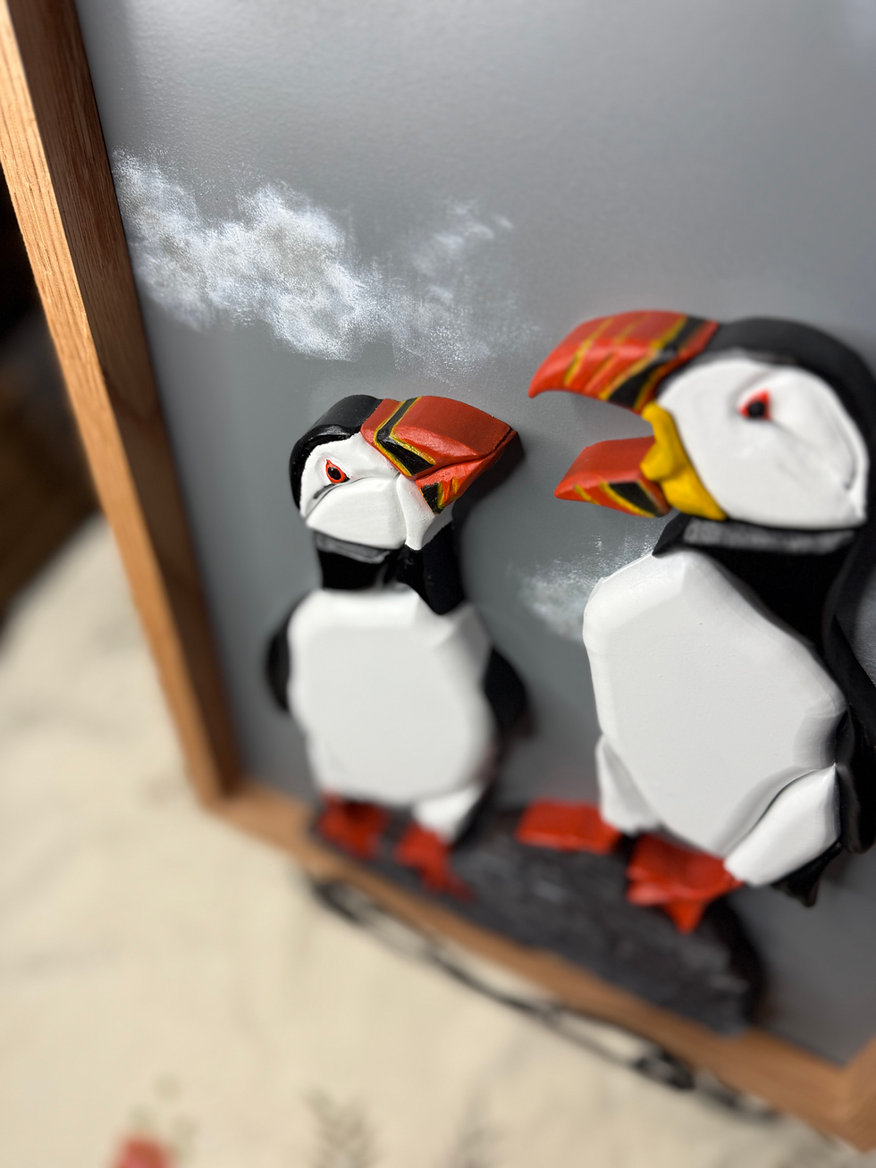 Thumbnail: Close up view of scroll saw cut, and painted wood puffins mounted on a hand painted backer and framed in solid oak.