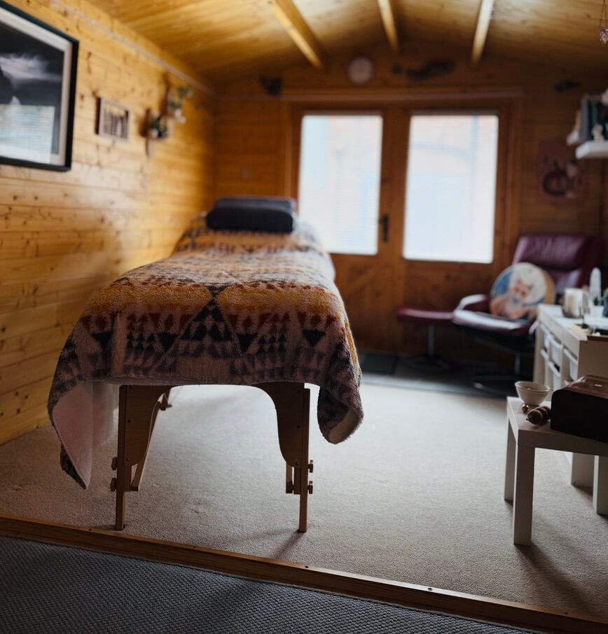 Reiki treatment couch inside the warm wooden Essential Energies treatment room with shamanic drums in the background