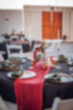 Close up of wedding reception set up. Black table cloths, red table runners, candles, green cloth napkins, plates and utensils.