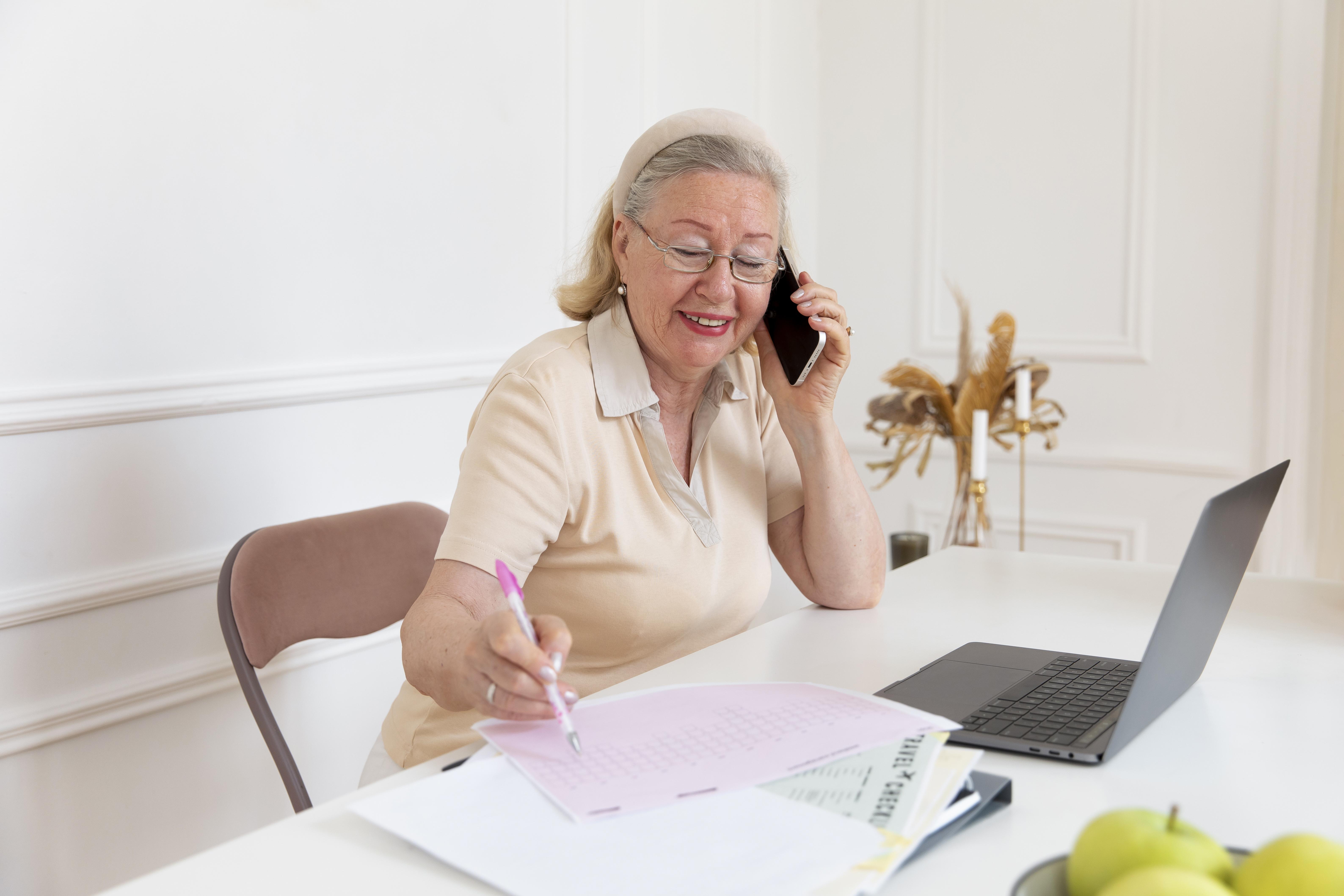 senior woman on phone call filling out paper work while smiling