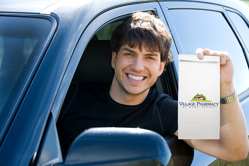 man smiling in the car with a village pharmacy prescription bag