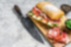 ciabatta-sandwich-with-prosciutto-crudo-ham-arugula-camembert-brie-cheese-gray-background-