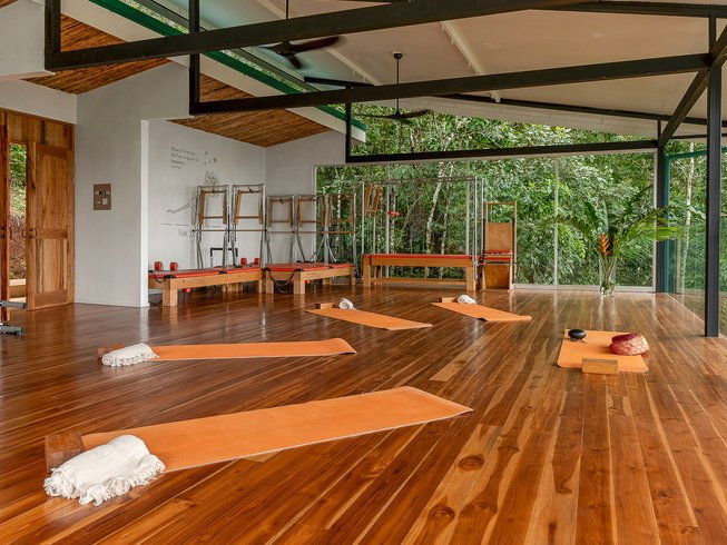 The best summer pilates retreat 2025 in Greece. People in a yoga class, stretching sideways on mats, in a bright room with white walls and large windows. Mood is focused and calm.