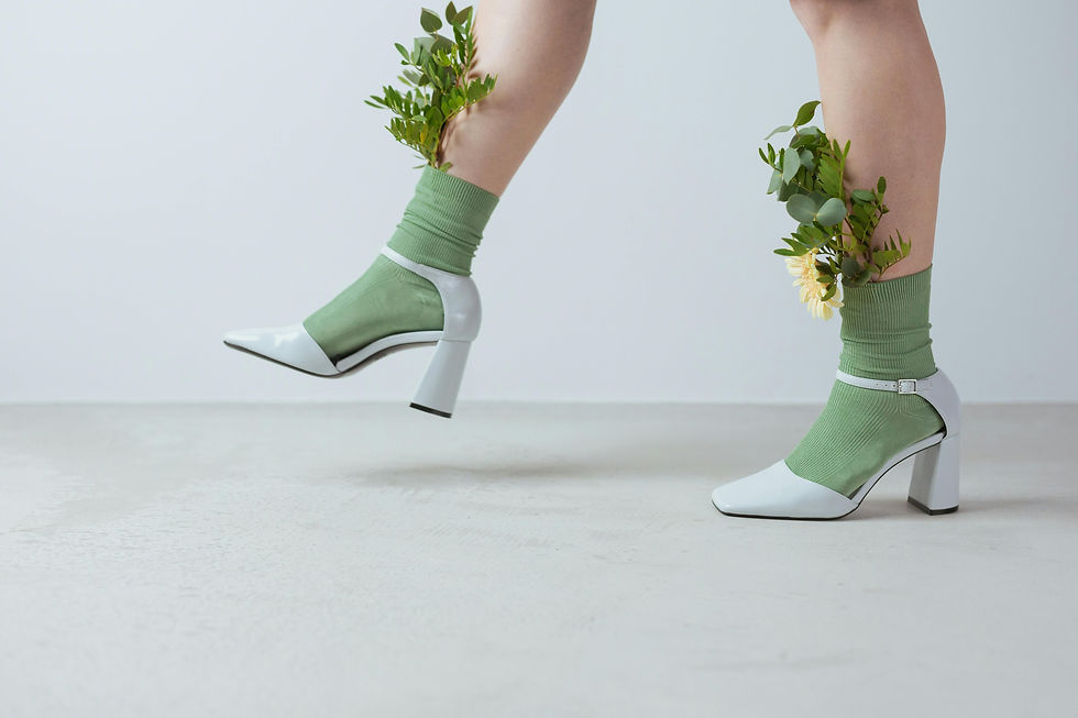 Legs wearing green socks with white heels, adorned with green leaves and flowers. Minimalistic setting with a neutral background.