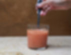 Hand stirring SuperRoot Anti-inflammatory juice in a glass with a metal spoon. Beige textured background and marble surface. Bubbles forming in the liquid.