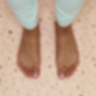 Two bare feet with light pink nail polish on a speckled pink mat. Person wearing light green pants. Calm setting. Before Yoga Toes Benefits