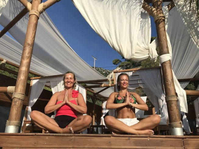 The best summer pilates retreat 2025 in France. Man in shorts performs a yoga pose on rocky sea shore at sunset, stretching arm and leg. Calm and focused expression, warm tones.