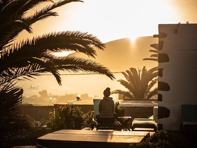 The best summer pilates retreat 2025 in Spain. Silhouetted person sitting outdoors at sunset, surrounded by palm trees. Warm, golden light creates a peaceful, reflective mood.
