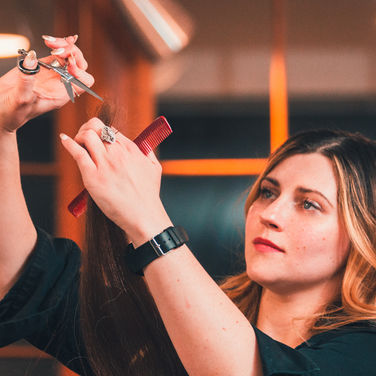 Clinical Trichologist Cosmetologist Kelsey Koldys performing haircut services adding layers to hair with red comb and determined happy face open evenings taking new clients