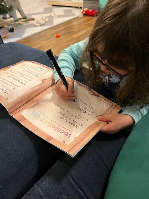 A young girl drawing on the vocabulary page of a book