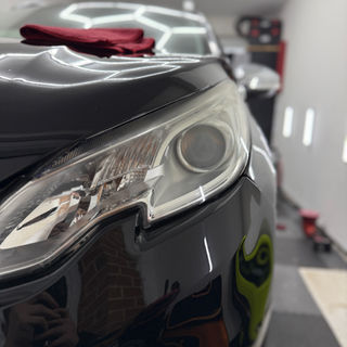 Shiny black car detail with bright lights in the background. Platform Auto Detailing