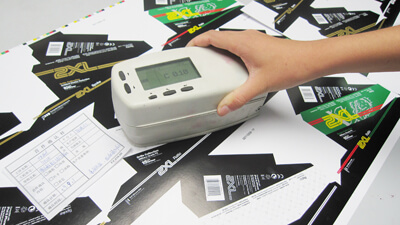 Technician measuring CMYK density with a densitometer on press sheets.