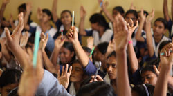 A large group of enthusiastic schoolgirls in uniform actively participate in a menstrual health educ