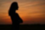 Silhouette of a woman with crossed arms against a vibrant orange sunset sky, conveying a contemplative mood and independence.