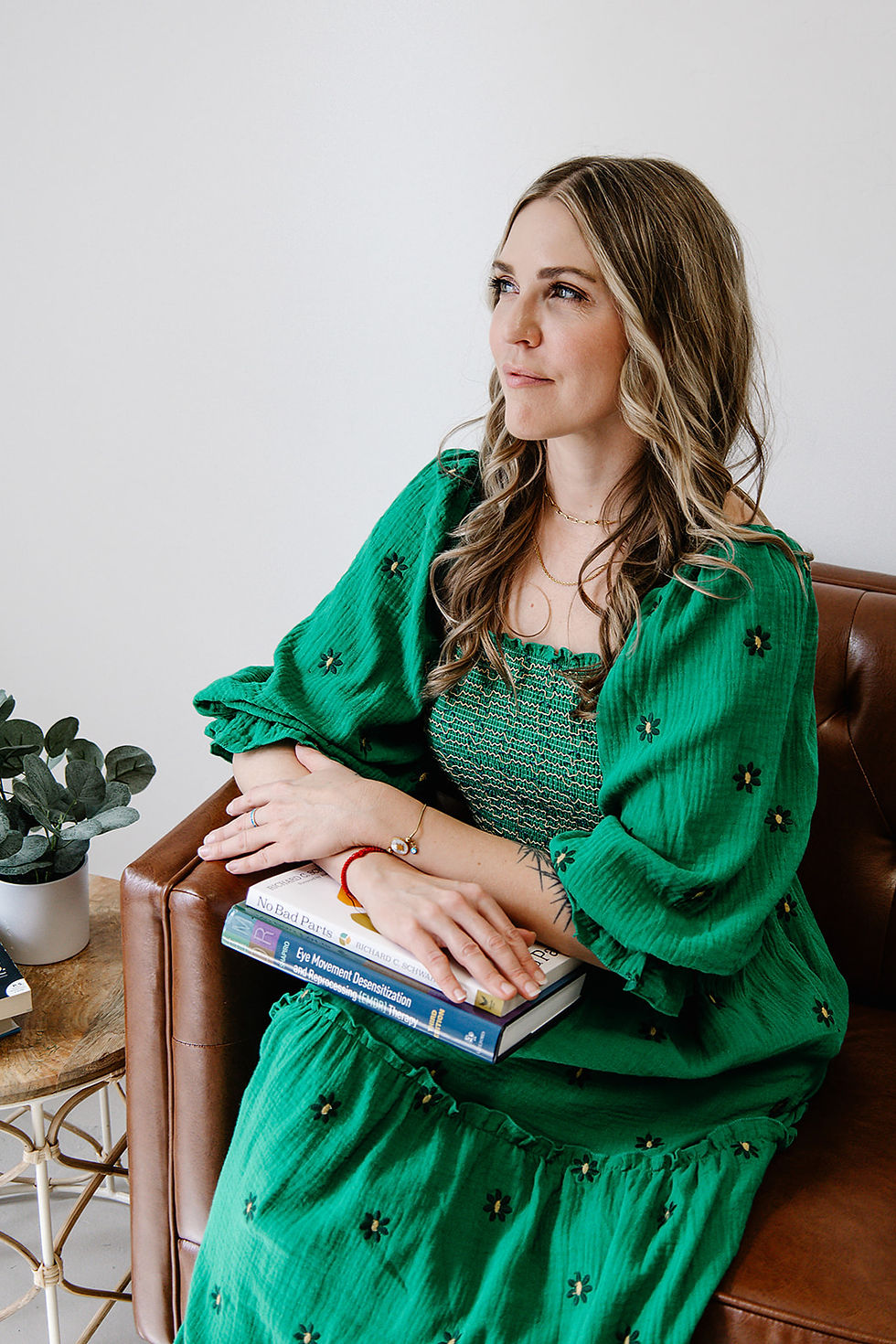 Picture of Alice Barclay, Licensed Counselor, seated on a couch looking off reflectively with a selection of therapeutic books on her lap including "No Bad Parts" by Richard Schwartz and the EMDR textbook by Francine Shapiro.