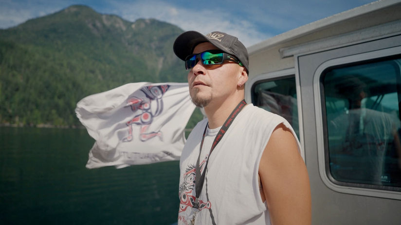 Person on boat, Tsleil-Waututh flag waving in wind behind him.