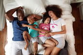 Photographie d'une famille allongée dans un lit passant un joyeux moment, ils sont habillés de tee-shirt et de short de la marque Gémo.