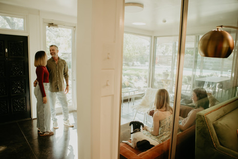 Mom and dad standing together with arms around each other near window light.