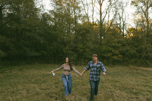 Couple running through a field together during maternity session with temple texas documentary photographer