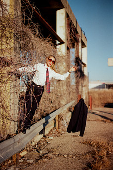 Woman dressed in a suit standing on the edge of a railing dropping a coat off onto the ground