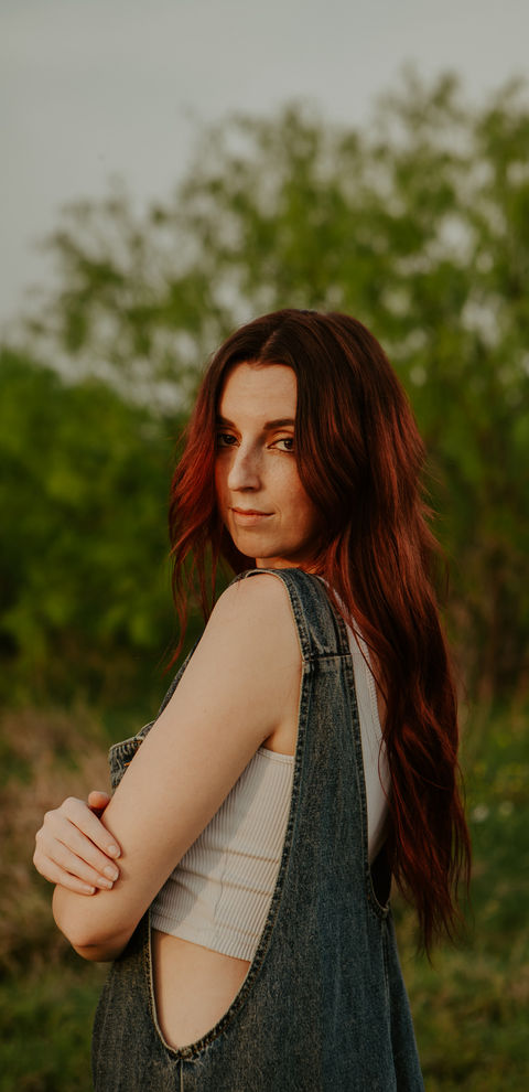 Young woman with red hair looking back, wearing overalls among greenery