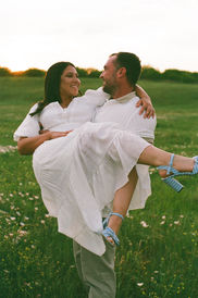 Man carrying woman laughing on a field; Couples + Engagements in a golden hour setting.