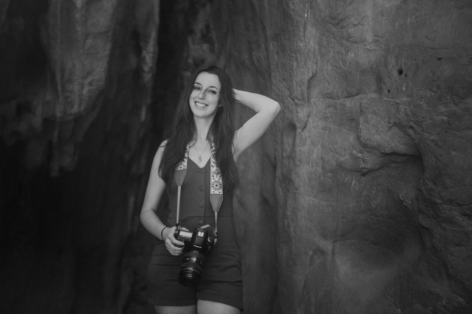 Smiling woman holding camera in front of a dark stone background