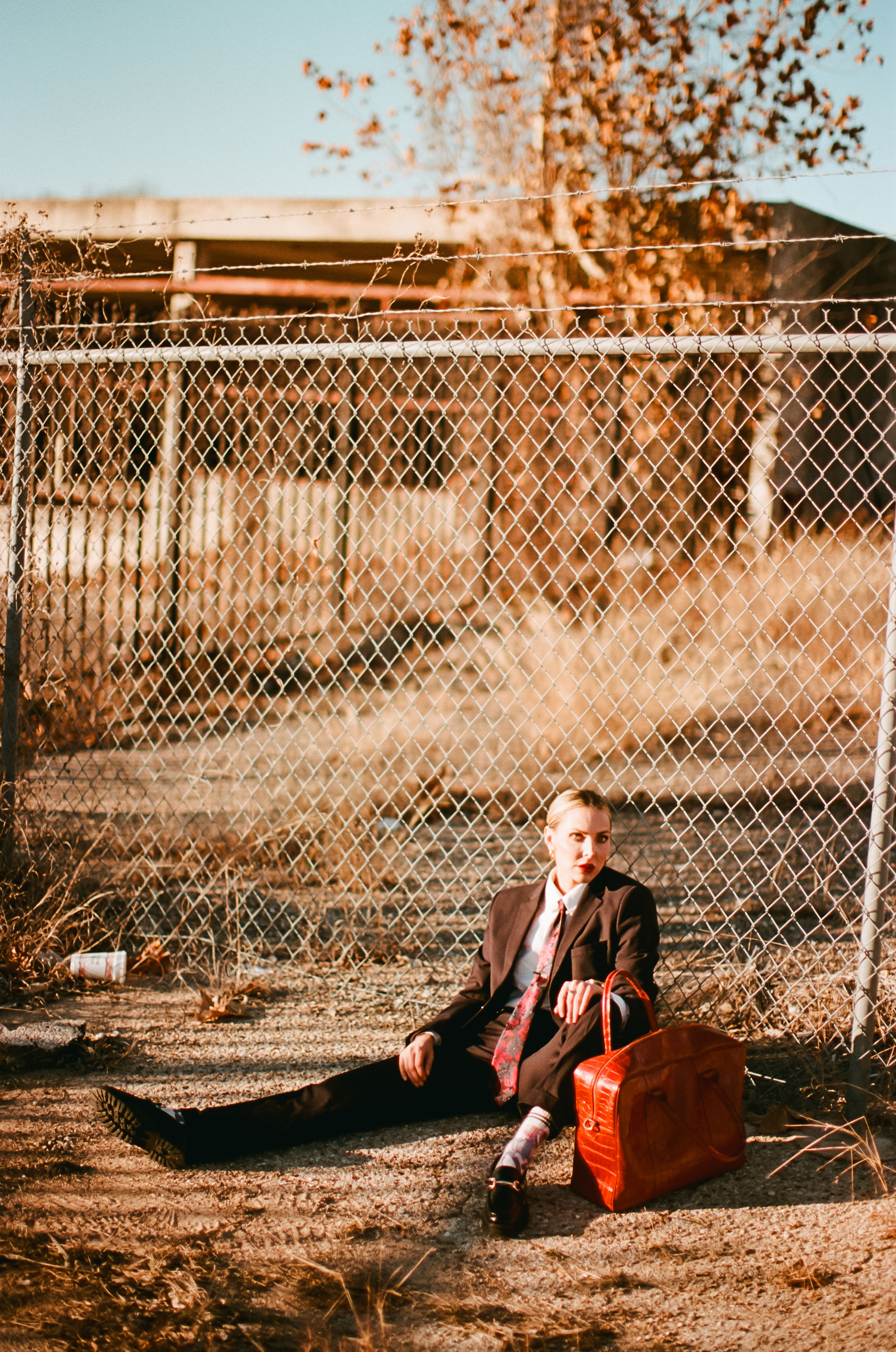 woman sitting on the ground leaning against a purse during central texas photoshoot at abandoned warehouse