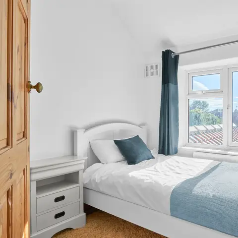 Property Photography North East is a folio of North Star Images
Specialising in Serviced accommodation photography, Interior Photography HMO Photography hartlepool
A calmming blue and white bedroom with warm wooden flooring
Bright, minimalist single bedroom with a white wooden bed, white bedding and teal throw blanket, matching teal curtains framing a sunlit window with neighborhood rooftop view, small white bedside table, light wooden door, and neutral walls creating a clean modern interior design.
This service acomadation marketing image was photographed by Property Photography North East a folio of North Star Images.