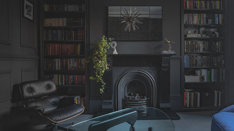 Moody and sophisticated living room with dark walls, built-in bookshelves, and a black fireplace as the focal point. A leather lounge chair, glass coffee table, and stylish decor elements, including a hanging plant and modern artwork, create a luxurious atmosphere. Expertly captured interior photography ideal for real estate, home design, and lifestyle branding. Photo by North Star Images.