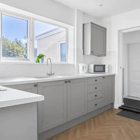 Property Photography North East is a folio of North Star Images
Specialising in Serviced accommodation photography, kitchen Photography HMO Photography Sunderland
A modern serviced accommodation kitchen featuring gray cabinetry, a white countertop, and a sink. A window provides natural light, and there's a microwave and kettle on the counter. A door leads to a hallway, and the floor has a herringbone pattern. This shows that a modern serviced accommodation kitchen photographed by property Photography North East a folio of North Star Images.