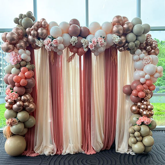 A balloon arch with pink, white, and gold balloons and flowers for an event