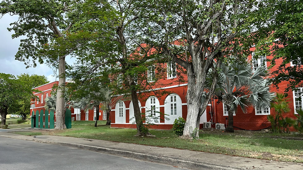 Red brick building with white-trimmed arched windows, surrounded by green trees and a sidewalk under a cloudy sky. No text visible.