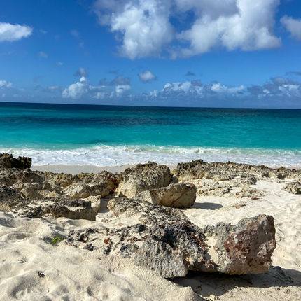 Rocky beach with turquoise ocean under a blue sky with clouds. Waves gently hit the shore, creating a calm and serene atmosphere.