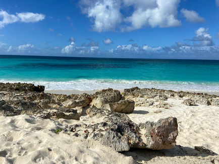Rocky beach with turquoise ocean under a blue sky with clouds. Waves gently hit the shore, creating a calm and serene atmosphere.