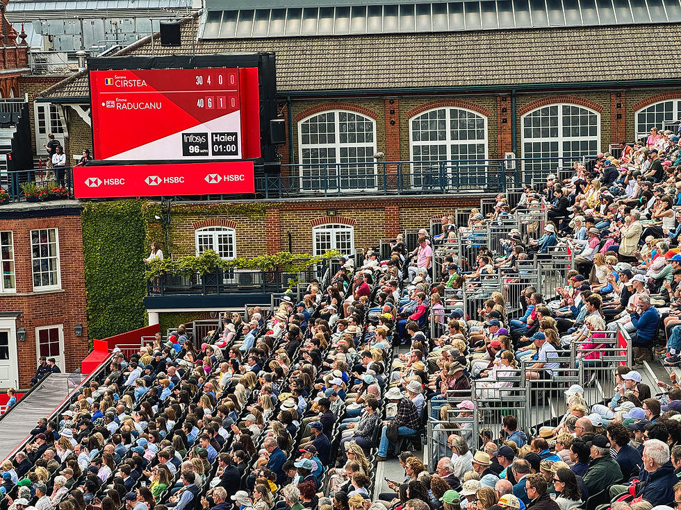 Crowded Wimbledon stands beneath a red scoreboard showing Cirstea vs Raducanu, with fans watching and clapping.