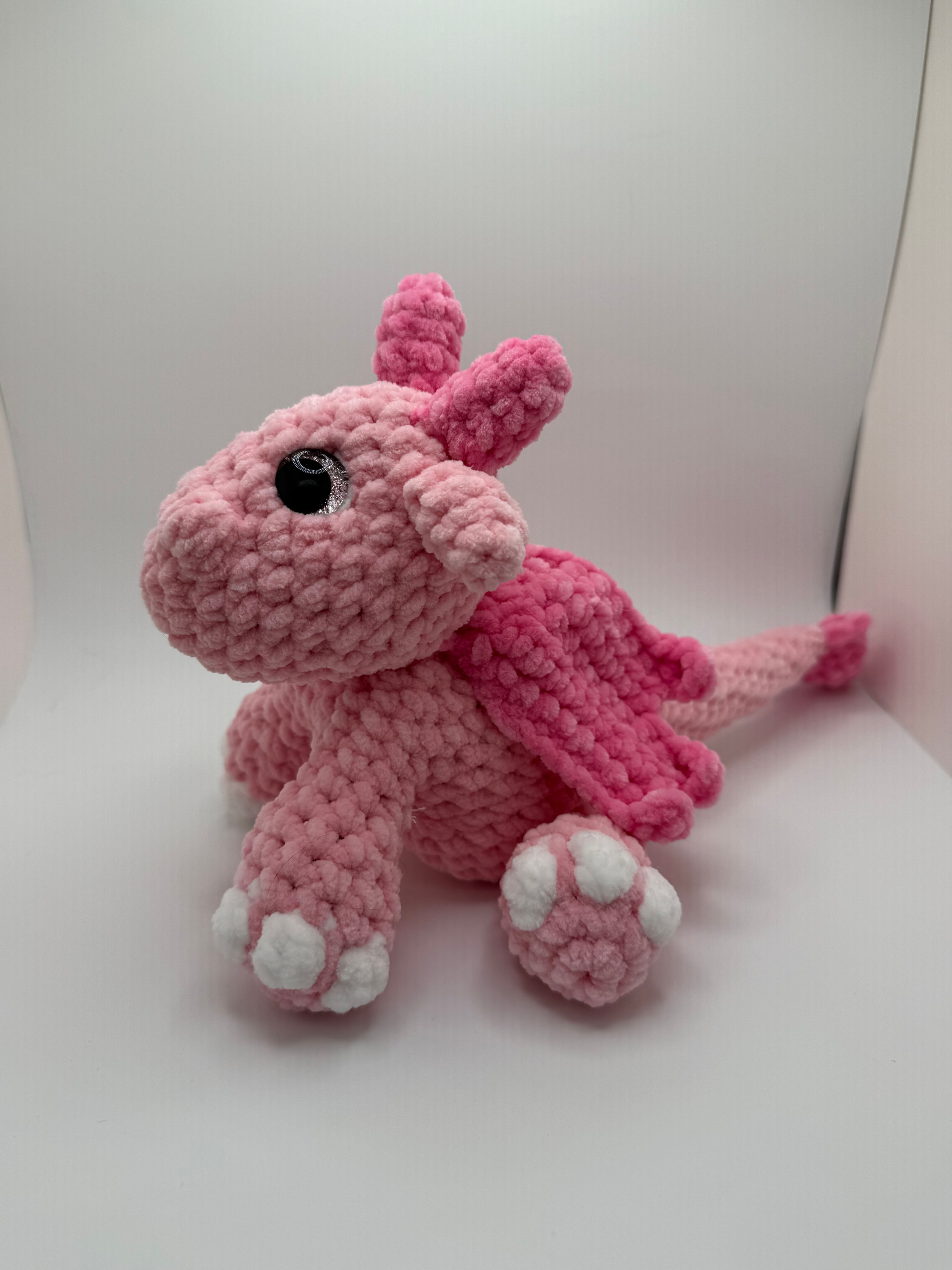 Small pink crocheted amigurumi dragon hatchling sitting