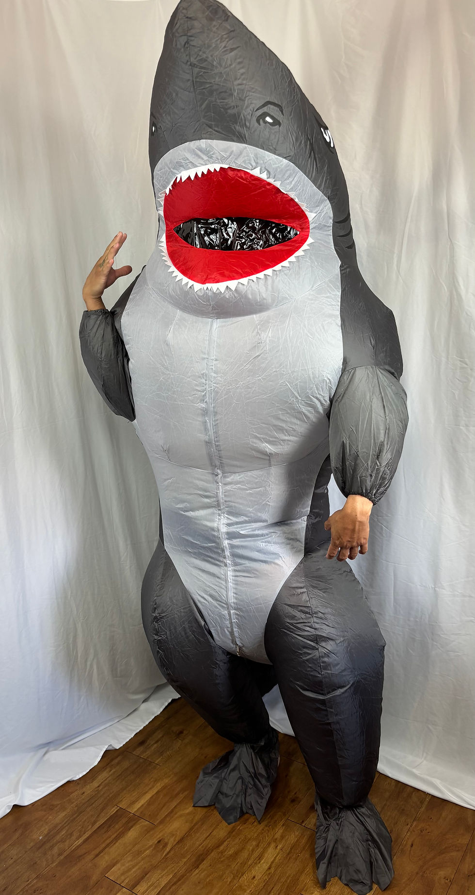 Front view of an adult wearing an inflated blue muscle shark mascot costume for a party.