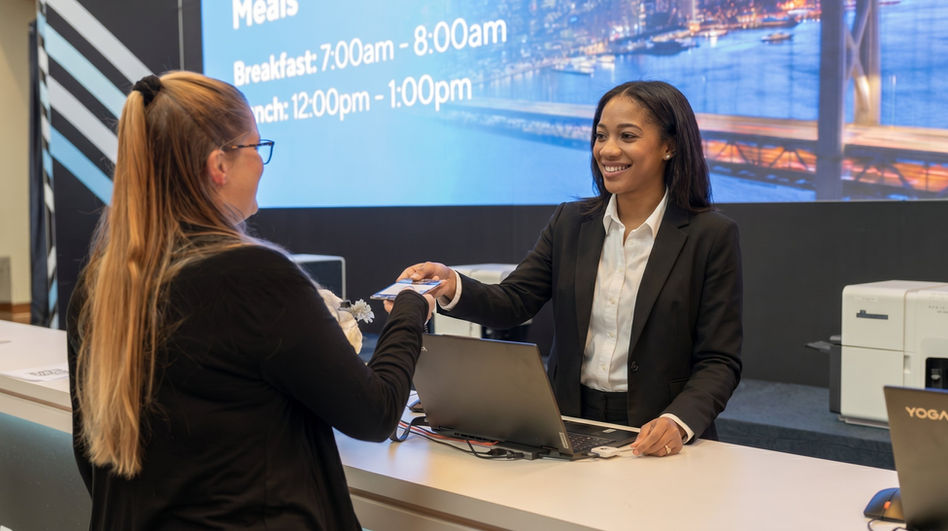Conference registration attendant assisting an attendee during a San Francisco business conference, supporting badge distribution, guest check-in coordination, and front-desk hospitality operations at a large-scale convention venue.