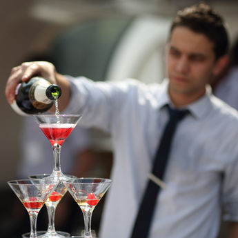 Event mixologist pouring cocktails into stacked martini glasses at a San Francisco event, showcasing refined beverage presentation for private parties, weddings, and corporate receptions across the Bay Area. The image highlights a mixologist focused on controlled pouring and visual appeal, creating a layered cocktail display that enhances the guest experience. Ideal for upscale events requiring creative drink styling, precise execution, and polished bar service that complements premium event environments.